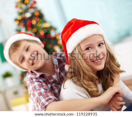 Portrait of happy girl looking at camera in her brother embrace on Christmas evening