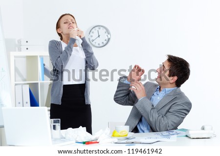 Image of sick businesswoman sneezing while her partner looking at her with anxiety in office