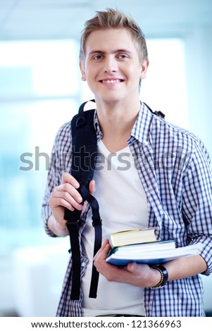 A young guy with backpack and textbooks looking at camera