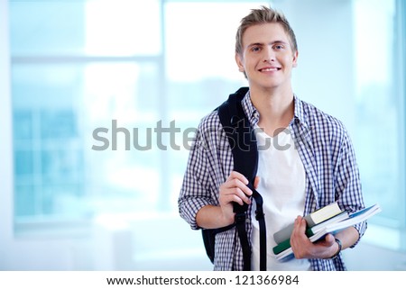 A young guy with backpack and textbooks looking at camera
