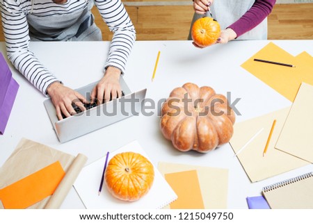 Unrecognizable busy designers working in art studio: woman painting Halloween pumpkin while man typing on laptop