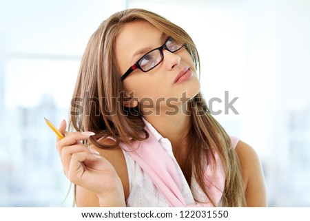 Portrait of pensive girl in eyeglasses holding pencil