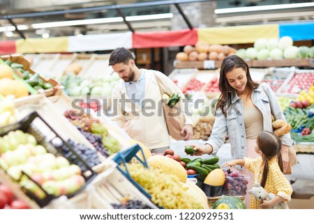 Cheerful beautiful young family in casual clothing walking over farmers market and buying food for dinner together
