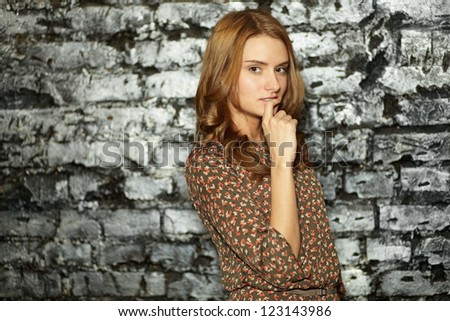Girl with a flirty look leaning against a grunge brick wall and looking at camera