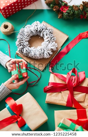 Overview of green table with various Christmas stuff and human hands holding small giftbox