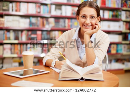 Portrait of clever student looking at camera and smiling in college library