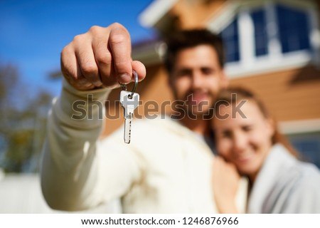 Key from new house in young man hand embracing his wife outdoors
