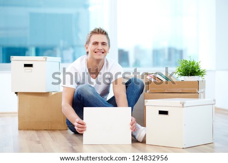 A young guy with blank paper sitting on the floor of new house surrounded with boxes