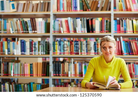 Portrait of clever student with open book looking at camera in college library