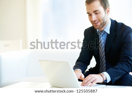 Portrait of attractive businessman in suit typing in office