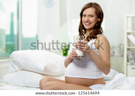 Photo of happy pregnant woman with glass of milk looking at camera