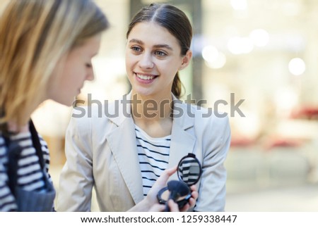 Young woman listening to shop assistant consultation about new facial powder while choosing cosmetics in beauty department