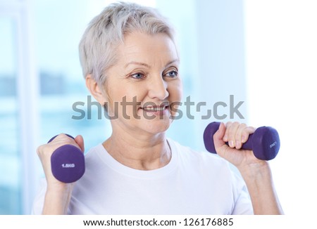 Portrait of pretty senior woman exercising with dumbbells