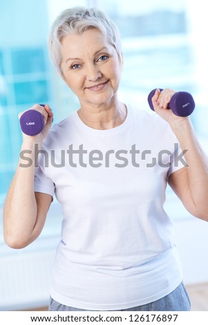 Portrait of pretty senior woman exercising with dumbbells