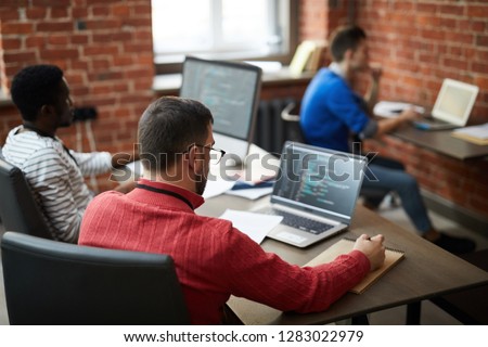 Group of contemporary it-engineers sitting b ydesks in front of computers and learning new software or codes