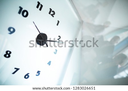 White clock in office or boardroom showing eleven minutes after ten and reflection of business team near by