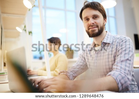 Bearded office manager in casualwear sitting in front of camera and analyzing online information