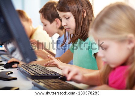 Portrait of lovely schoolgirl looking at computer keyboard while typing