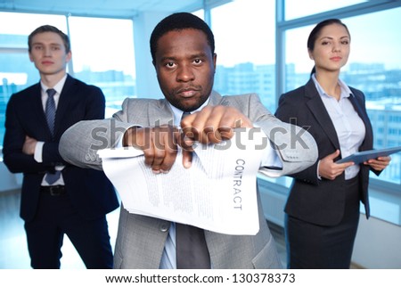 Portrait of African businessman tearing contract while looking at camera with two partners on background