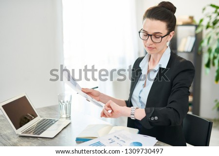 High angle portrait of successful young businesswoman looking at watch while working in office, copy space