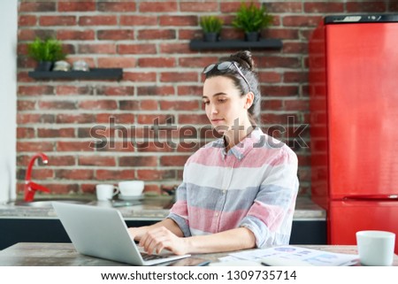 Portrait of modern young woman using laptop at home doing blogging or freelance work