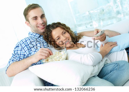 Young lovers enjoying lazy weekend watching TV and eating pop-corn
