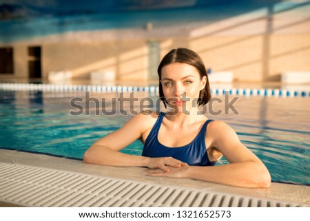 Young brunette fit woman looking at you while standing in water after swim training in sports center