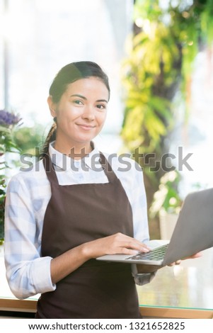 Happy successful staff or owner of florist shop with laptop looking at you while browsing in the net