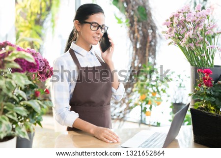 Young assistant of contemporary florist shop consulting clients on smartphone and online
