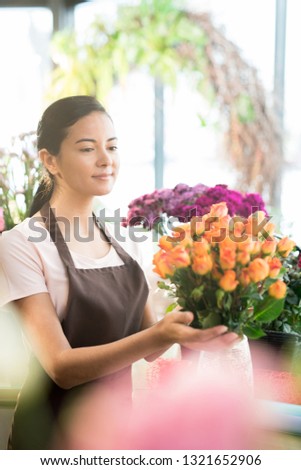 Young pretty florist making big bouquet of fresh orange roses while preparing it for one of clients