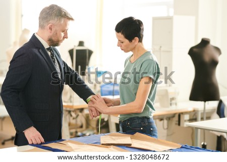 Professional seamstress in casualwear taking measures of client wrist before making new suit for him