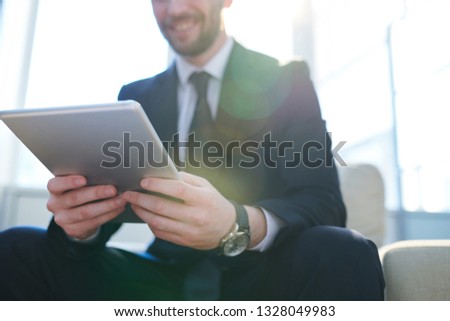 Contemporary business employee in formalwear holding touchpad while surfing in the net for ideas