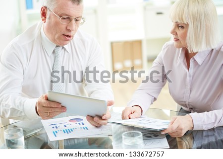 Two mature business partners working with paper and electronic documents at meeting