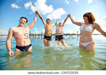 Photo of happy family standing in water and having fun on summer day