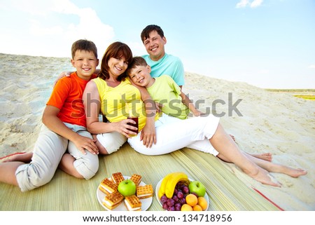 Photo of happy family sitting on sand and having lunch during summer rest