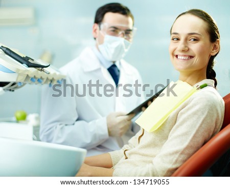 Smiling woman sitting in dentistÃ?ÃÂ¢??s chair with doctor on background