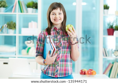 Teenage girl with notepad and green apple looking at camera with smile