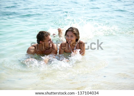 Young joyful couple lying in water and splashing playfully