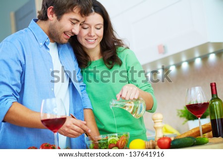 Portrait of young man and his wife seasoning salad with oil in the kitchen