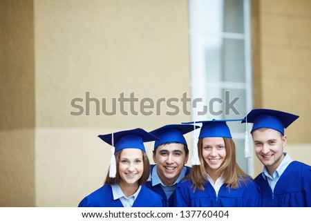 Group of smart students in graduation gowns looking at camera