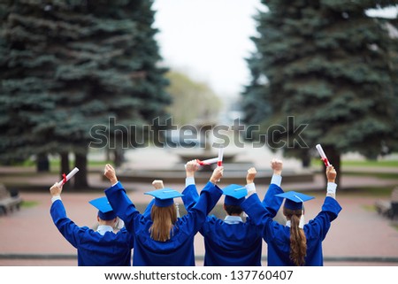 Backs of ecstatic students in graduation gowns holding diplomas Backs of ecstatic students in graduation gowns holding diplomas