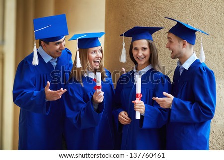 Group of smart students in graduation gowns having chat