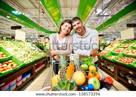 Image Of Happy Couple With Cart Full Of Products Looking At Camera In Supermarket