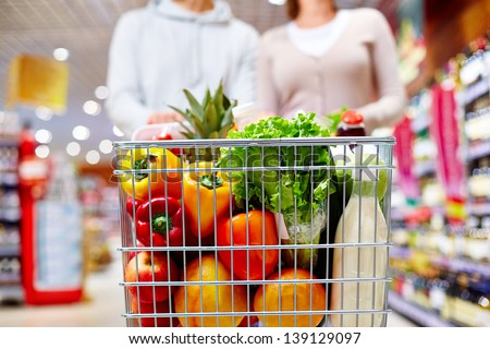 Image Of Cart Full Of Products In Supermarket Being Pushed By Couple