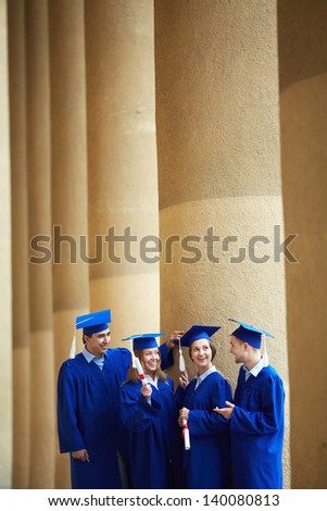 Group of smart students in graduation gowns having chat