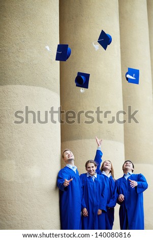 Group of smart students in graduation gowns throwing their hats