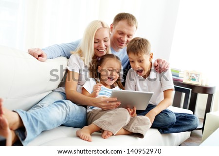 Portrait of ecstatic family with two children looking at something funny in touchpad