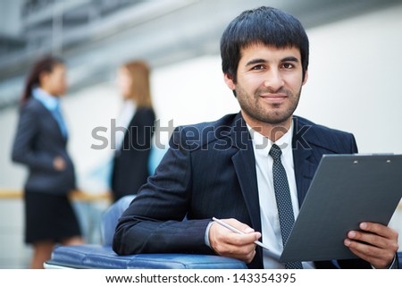 Portrait of confident male leader with clipboard looking at camera in working environment