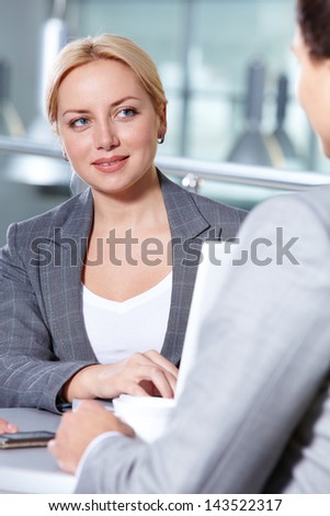 Portrait of pretty woman at workplace looking at her business partner while speaking to him