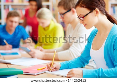 Portrait of pretty girl sitting in college library and making notes